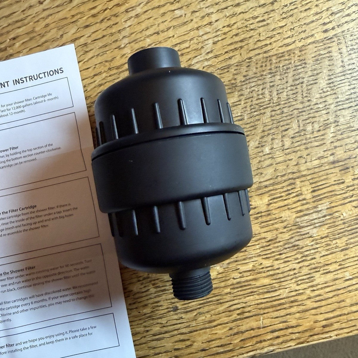 Real photo of the matte black shower filter unboxed on a table beside its instruction sheet